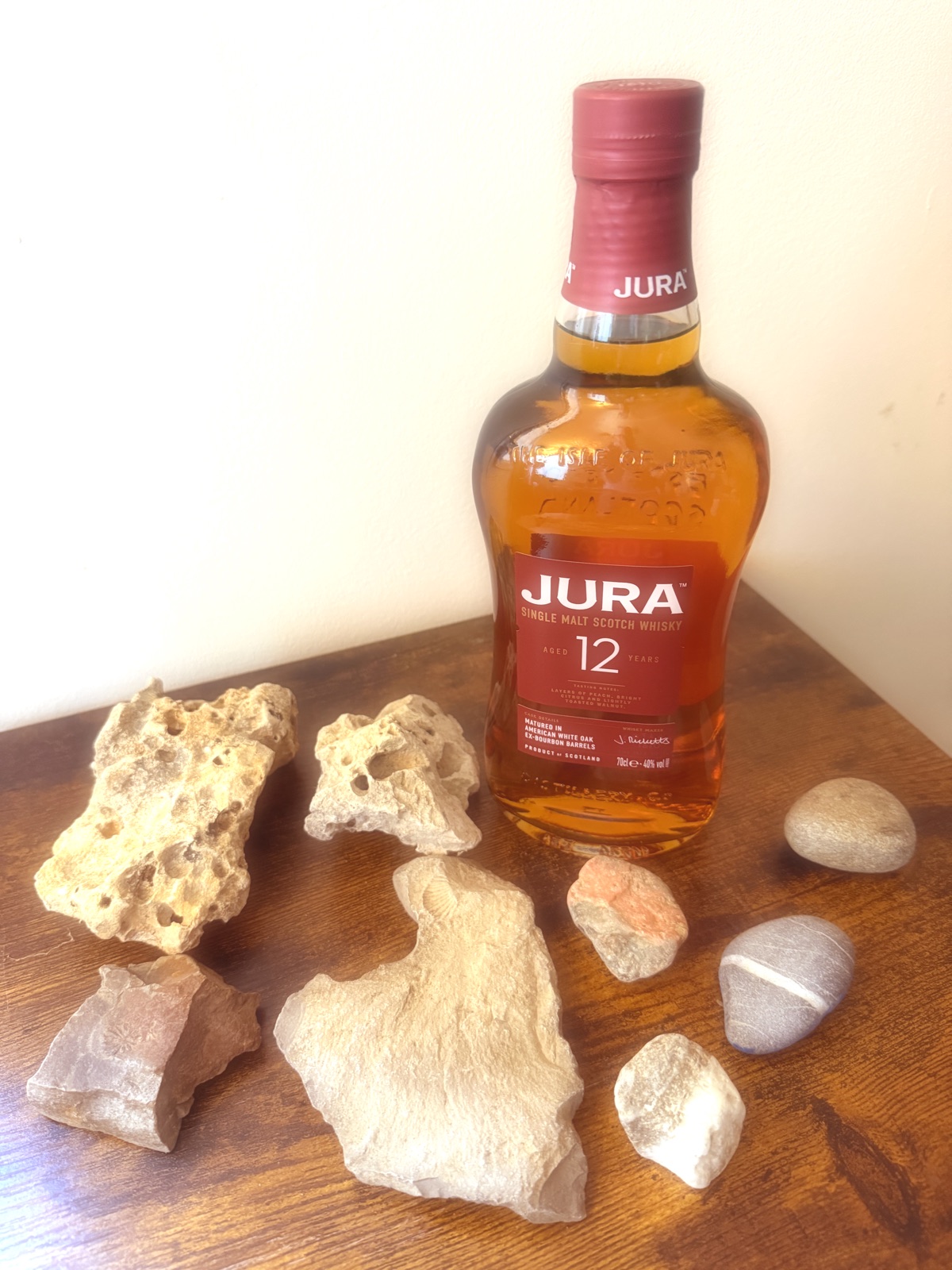 Bouteille de Jura 12 ans sur un bois sombre, entourée de pierres claires à fossiles et de galets polis